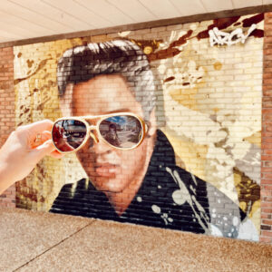 Courtesy Tupelo CVB A person holding up sunglasses on the eyes of Elvis Presley in Tupelo, Miss.