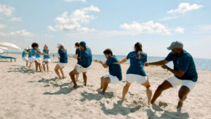 A group of meeting attendees play tug-of-war on the beach.