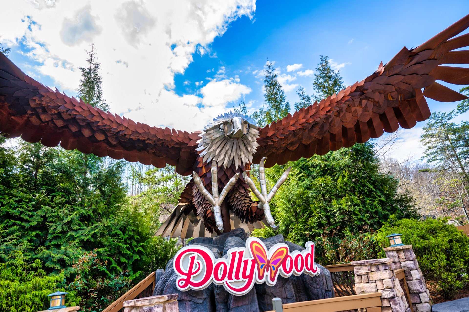 Dollywood sign beneath a timber canopy, with trees and blue sky in the background.